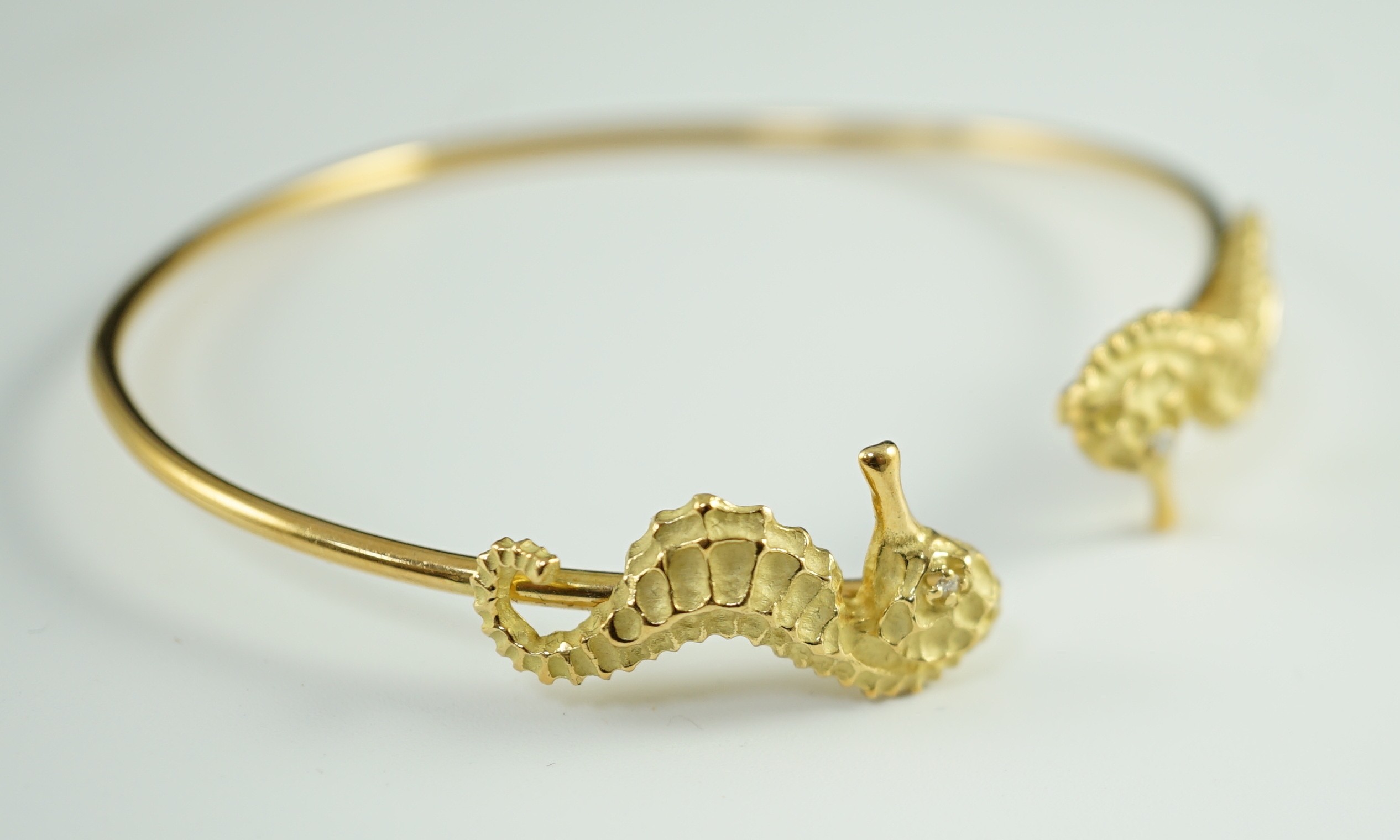 A modern gold and diamond chip set open work bangle, each terminal modelled as a seahorse with diamond chip eye